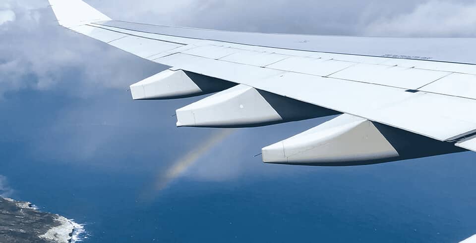 white wing of an airplane over a body of water with a rainbow in the distance