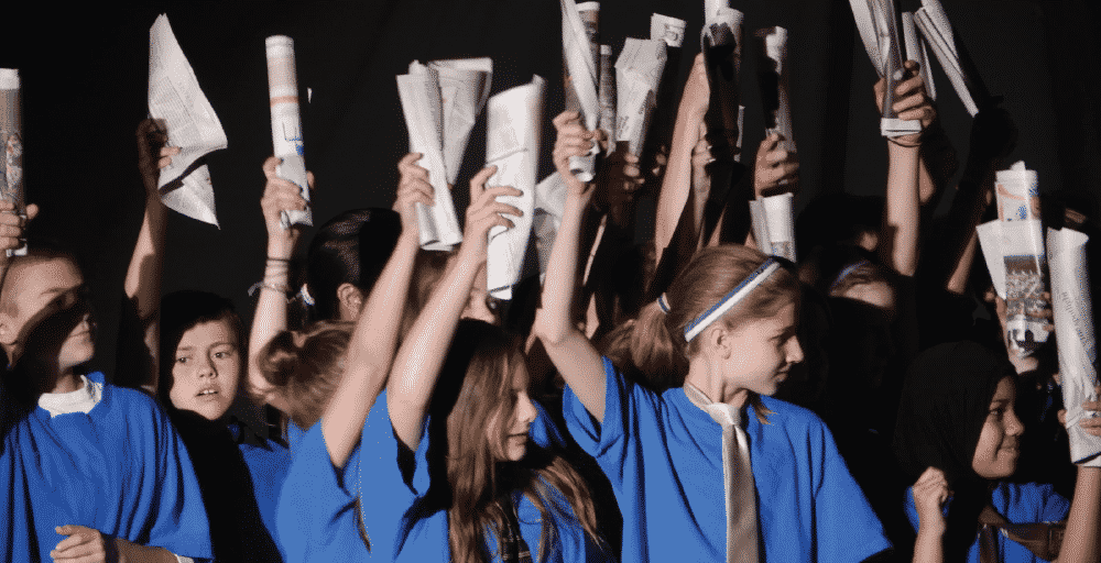 children in blue shirts hold blue shirts and hold newspapers up in the air