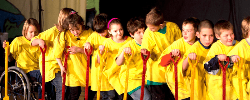 children dressed in yellow shirts hold red shovels